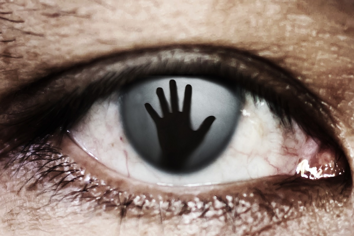 An eye with the reflection of a raised hand showing in the middle.